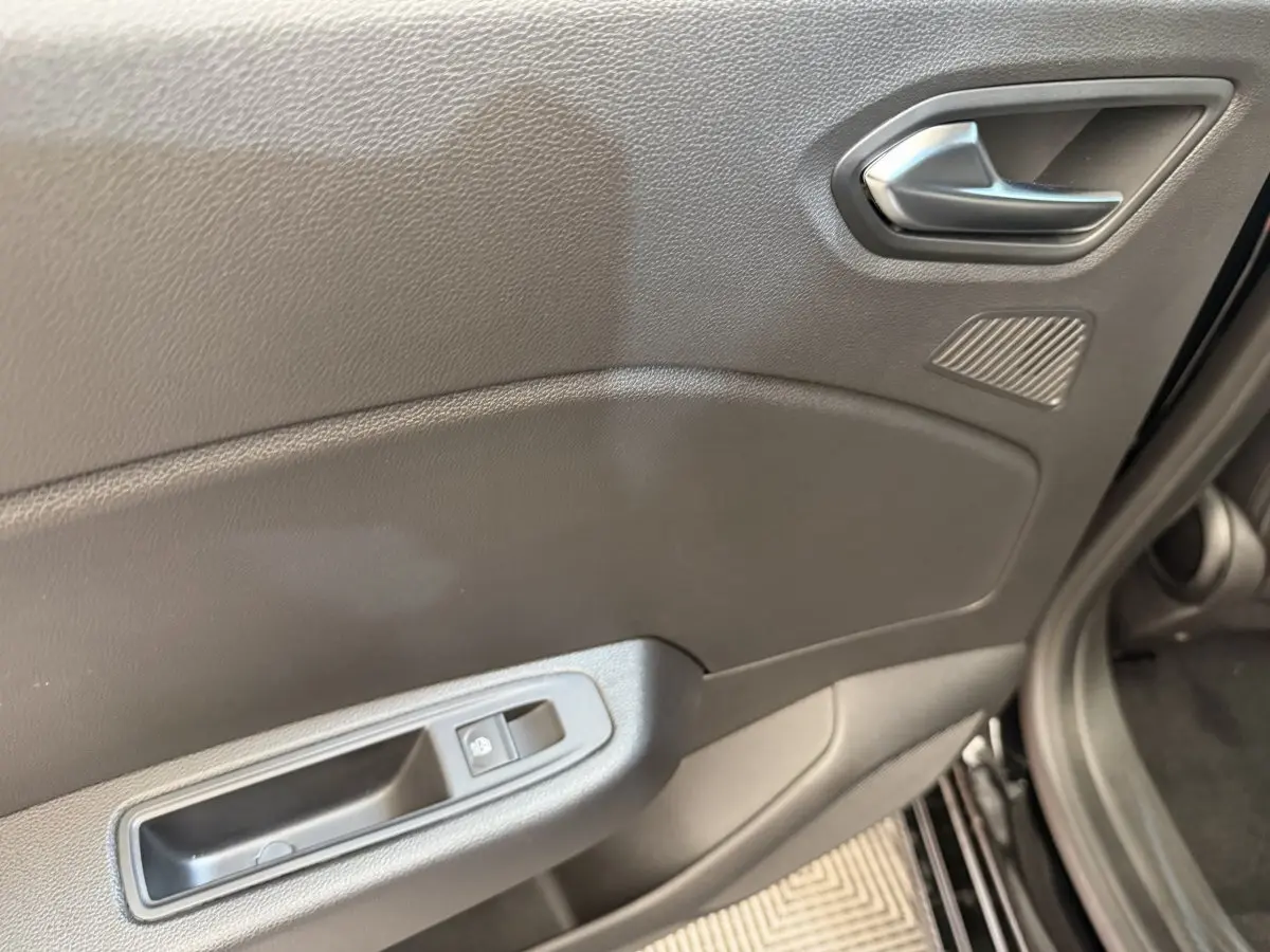 Gros plan sur la porte intérieure côté droit de la Renault Clio noire, avec poignée argentée et commande de fenêtre électrique.