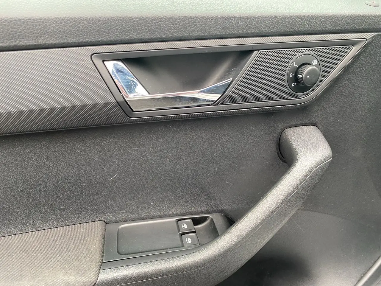 Gros plan sur la poignée intérieure côté gauche de la porte d'une Skoda Fabia gris argent, avec commandes de vitres et réglage des rétroviseurs.