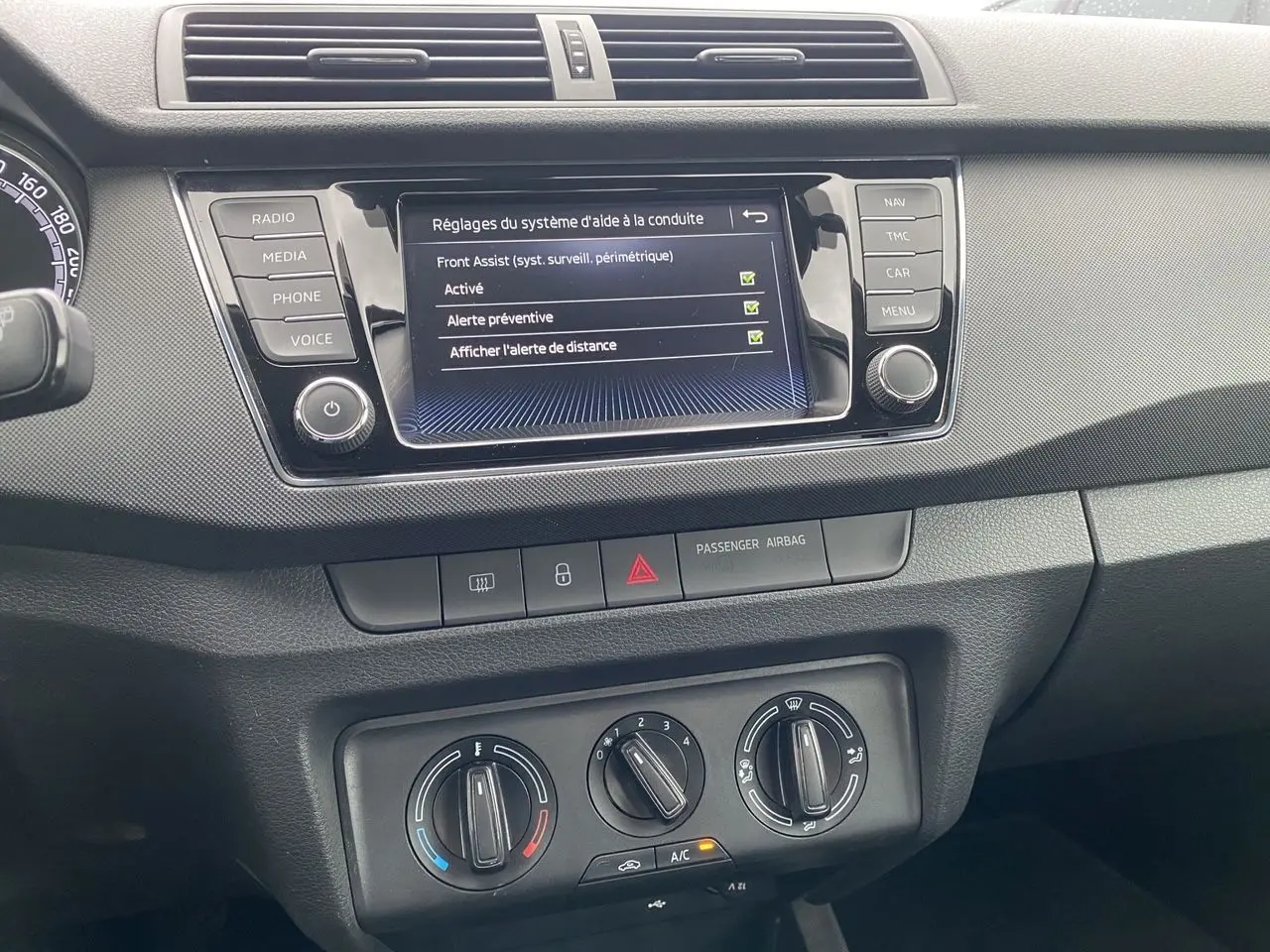 Vue rapprochée du tableau de bord gris argent d’une Skoda Fabia 2021, avec écran multifonction affichant les réglages d’aide à la conduite.