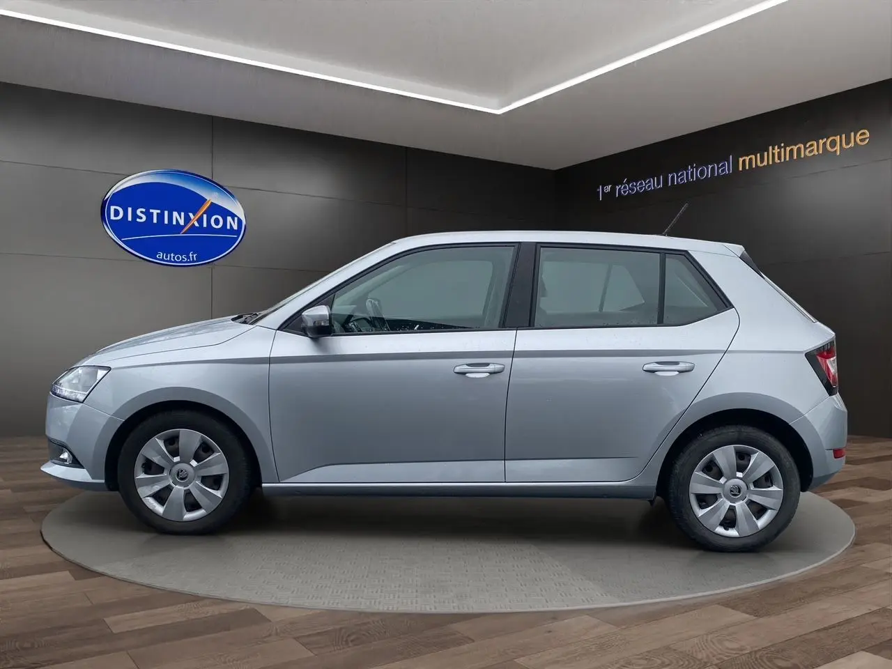 Vue de profil côté gauche d'une Skoda Fabia gris argent 2021 en finition Business, présentée en showroom.