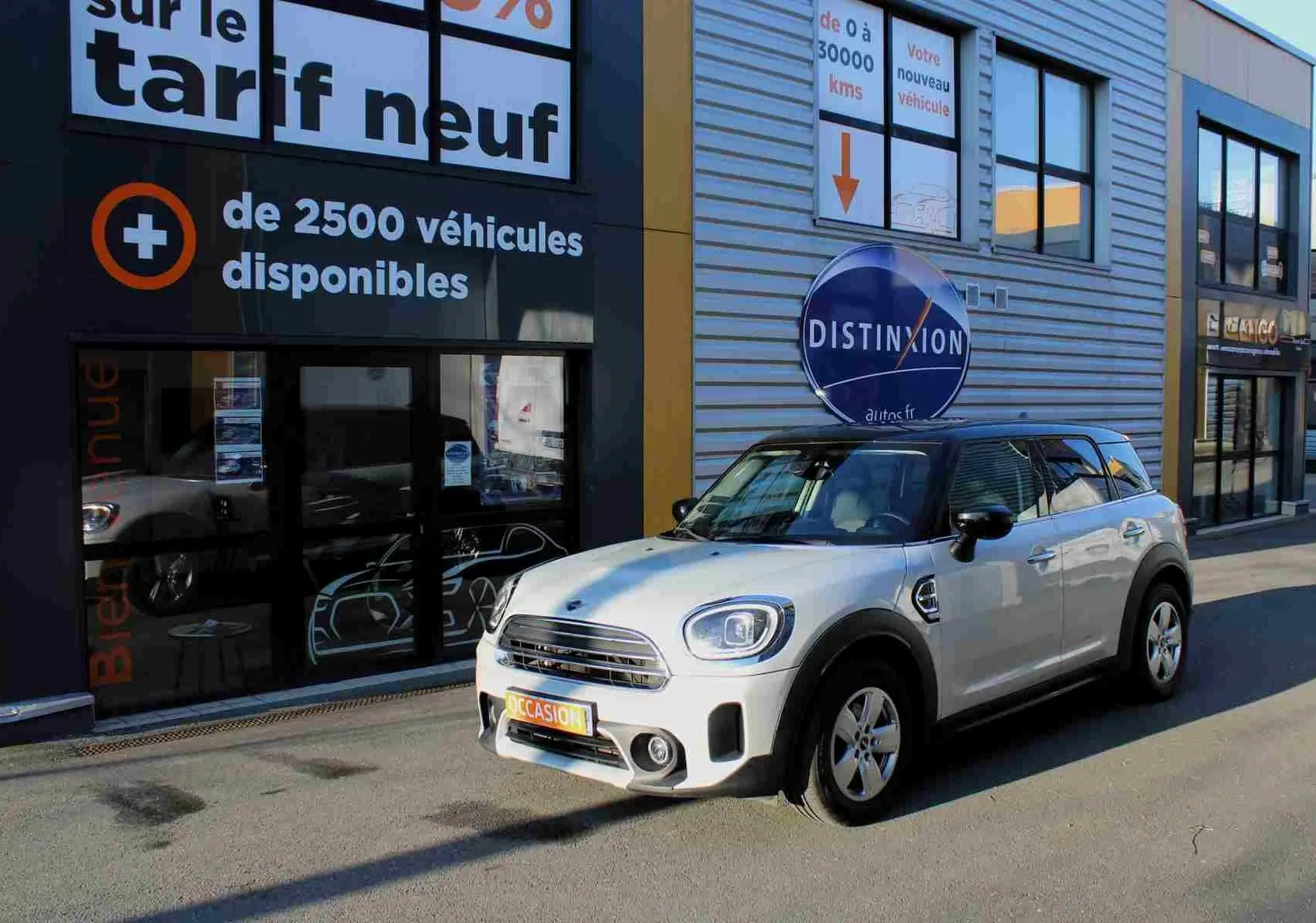 MINI Countryman gris perle métal avec toit noir, vue 3/4 avant droit devant un bâtiment commercial.