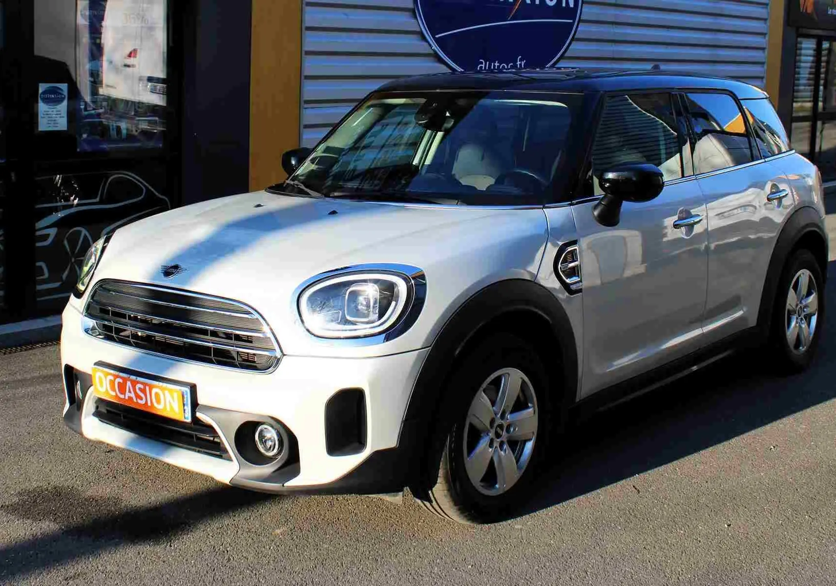 MINI Countryman gris perle métal avec toit noir, vue 3/4 avant droit, garée devant un bâtiment commercial.