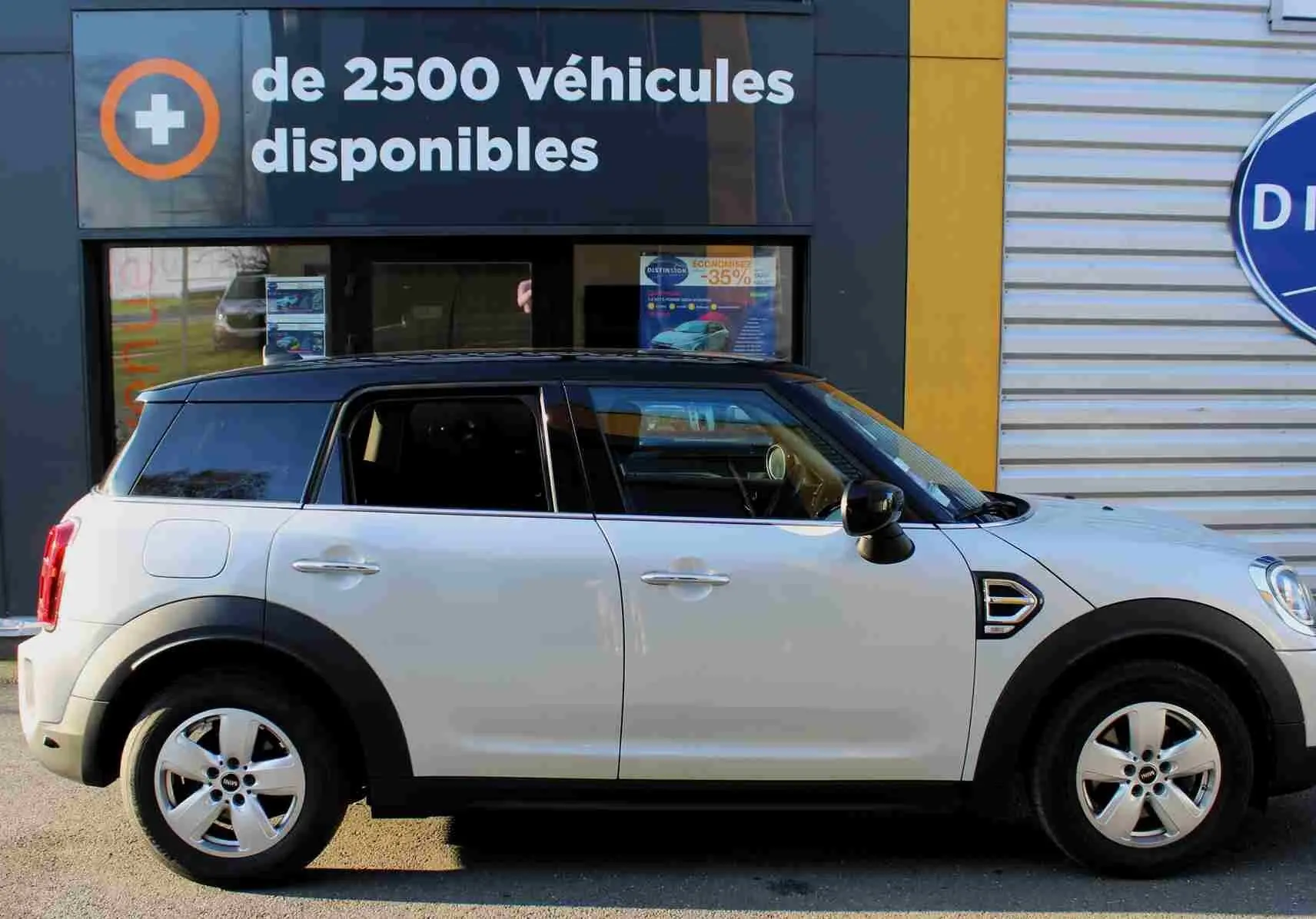 Profil droit d'un MINI Countryman gris perle avec toit noir, roues alliage et protections noires autour des passages de roues.