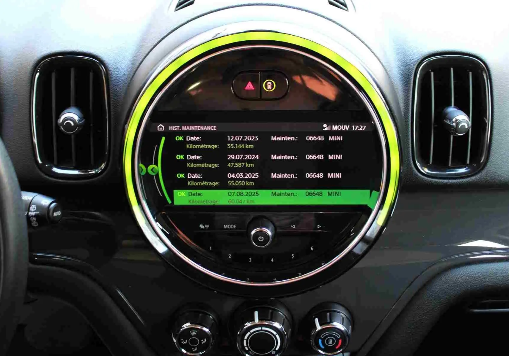Vue rapprochée du tableau de bord central noir du MINI Countryman avec écran rond affichant l'historique de maintenance.