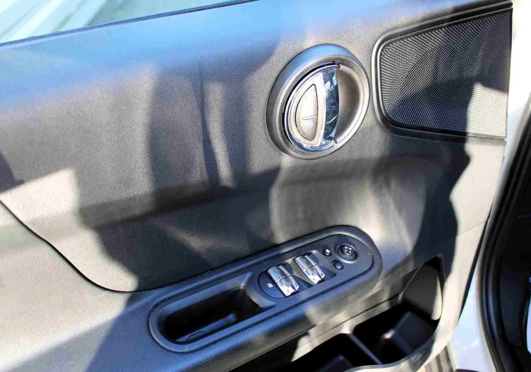 Gros plan sur la porte avant gauche intérieure du MINI Countryman gris perle, avec commandes de vitres et poignée chromée.