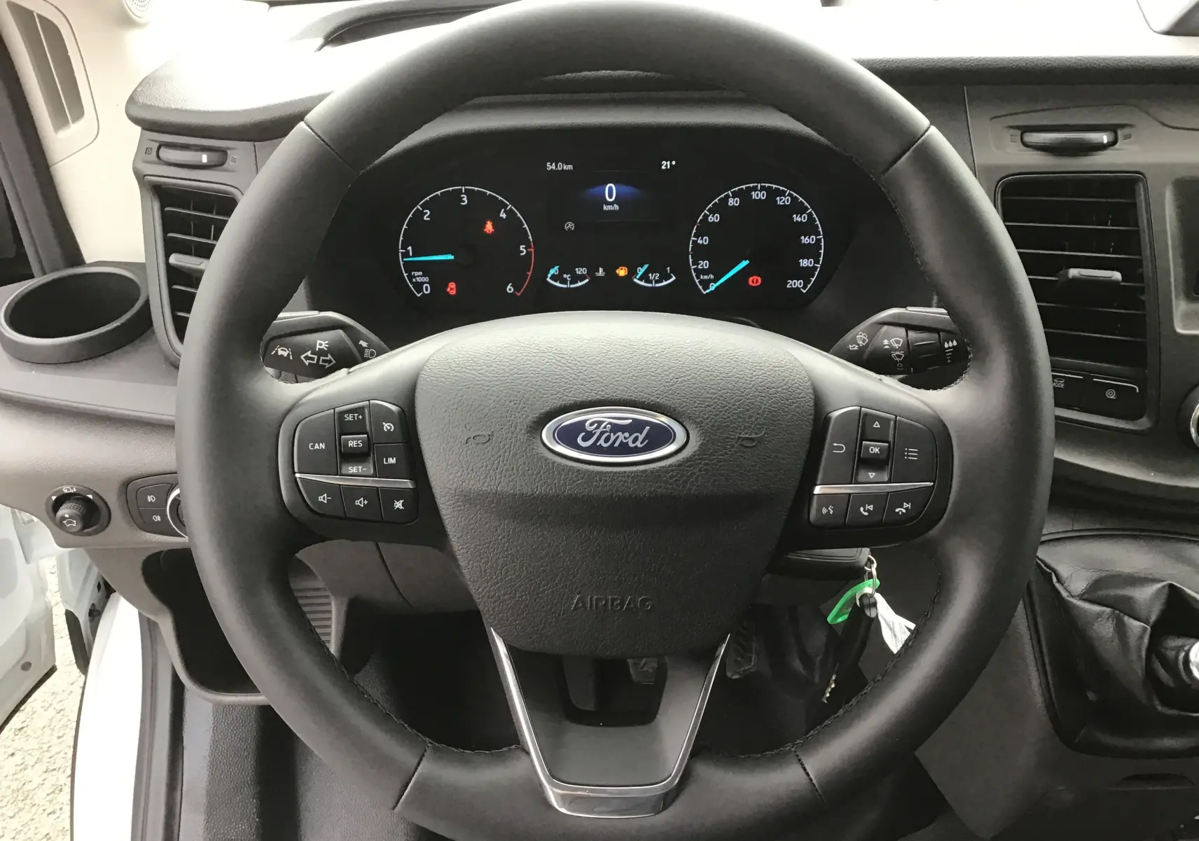 Vue rapprochée du volant Ford noir avec commandes intégrées et tableau de bord numérique du Transit Chassis Cabine blanc.