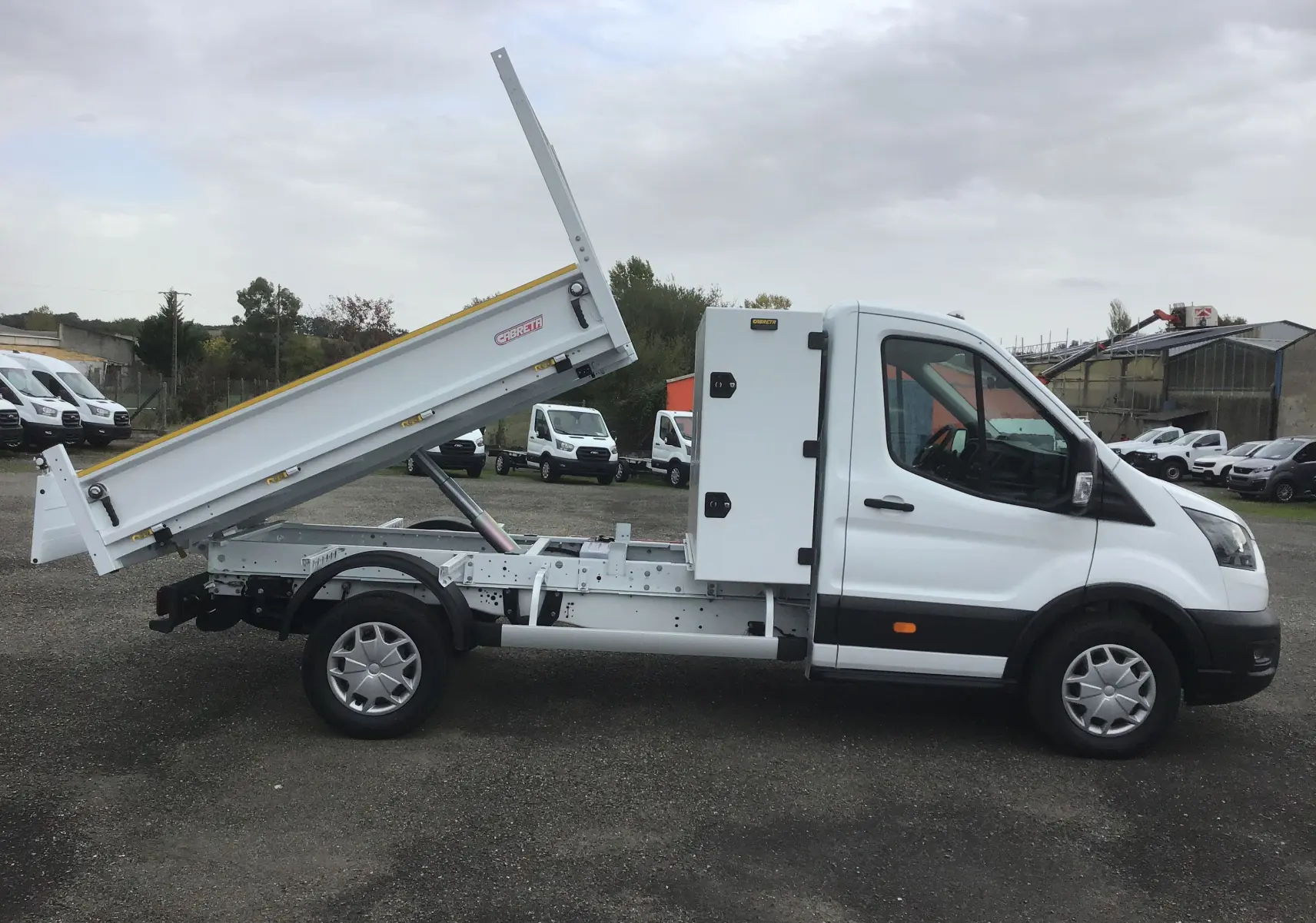 Ford Transit Chassis cabine blanc vu de profil droit, avec benne relevée et coffre latéral acier.