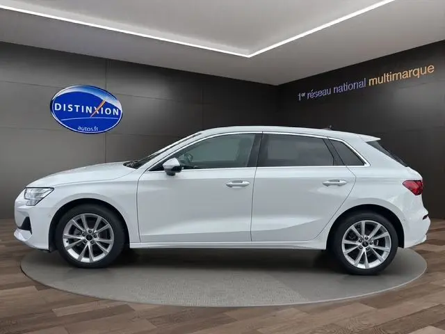 Vue latérale droite d'une Audi A3 Sportback 2024 blanc Arkona avec jantes alliage et vitres teintées, en showroom.