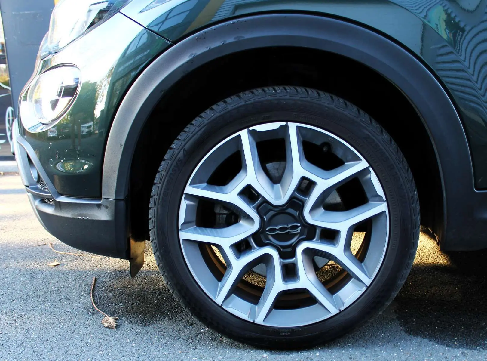 Gros plan sur la roue avant gauche d'une FIAT 500X vert Toscane métal, mettant en valeur la jante alu au design moderne.