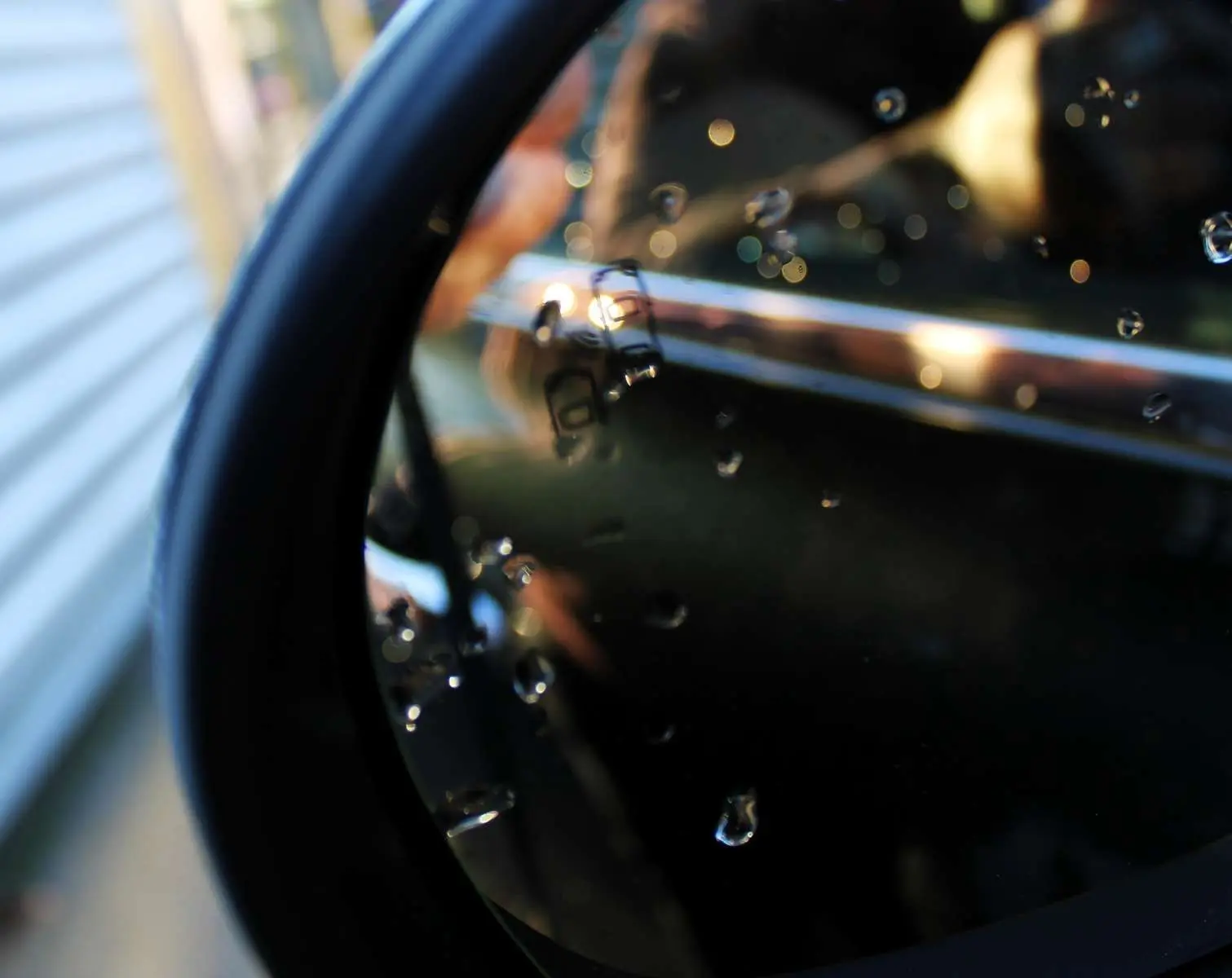 Gros plan sur la poignée chromée et la vitre arrière d'une FIAT 500X vert Toscane sous gouttes d'eau.