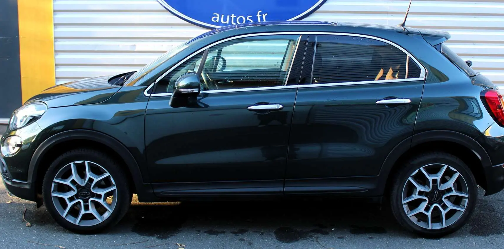 Profil côté gauche d'une FIAT 500X vert Toscane métal 2019 avec jantes alliage et attelage visible.