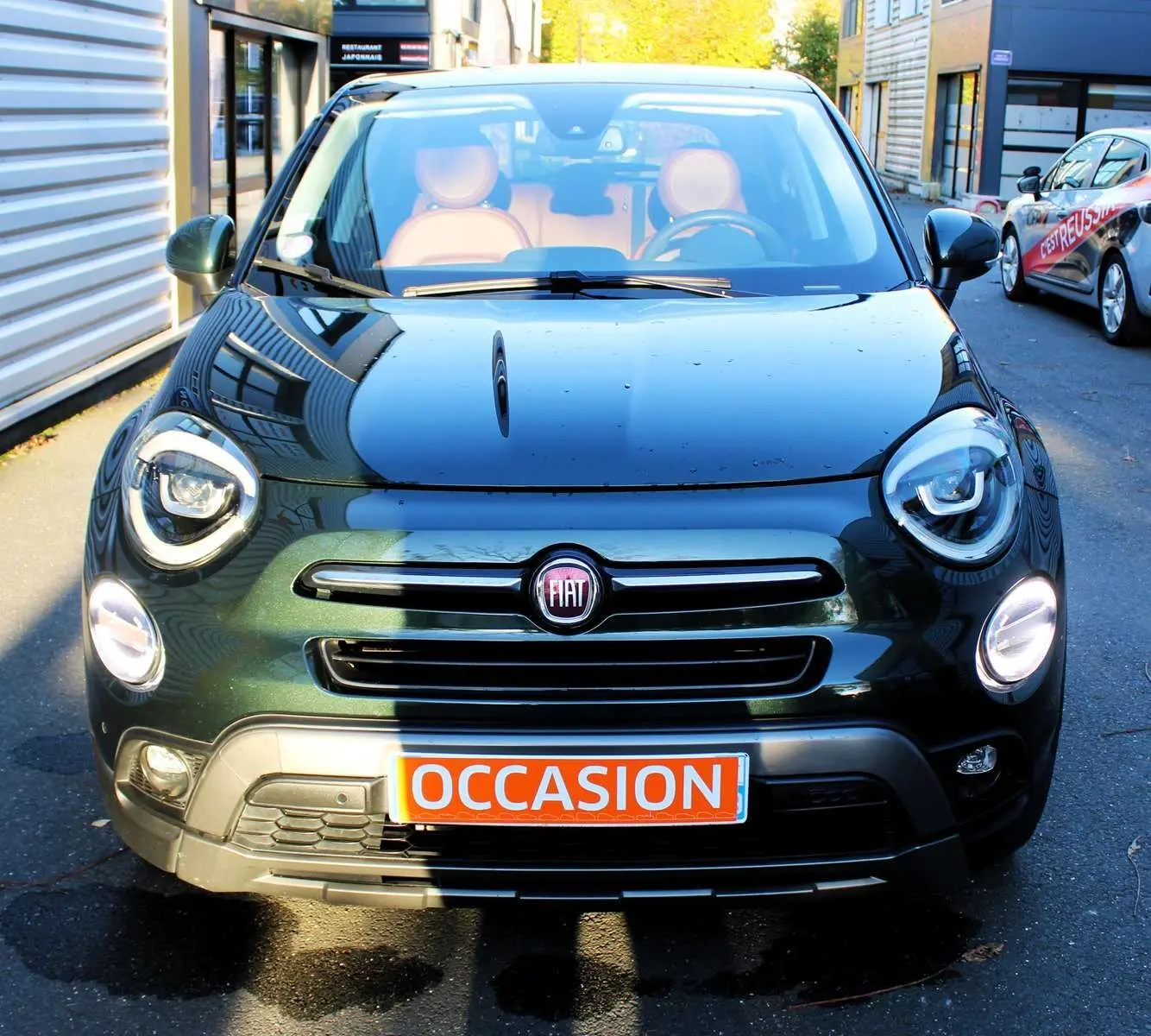 Vue de face d'une FIAT 500X vert Toscane métallisé avec intérieur cuir marron et plaque "OCCASION" visible.