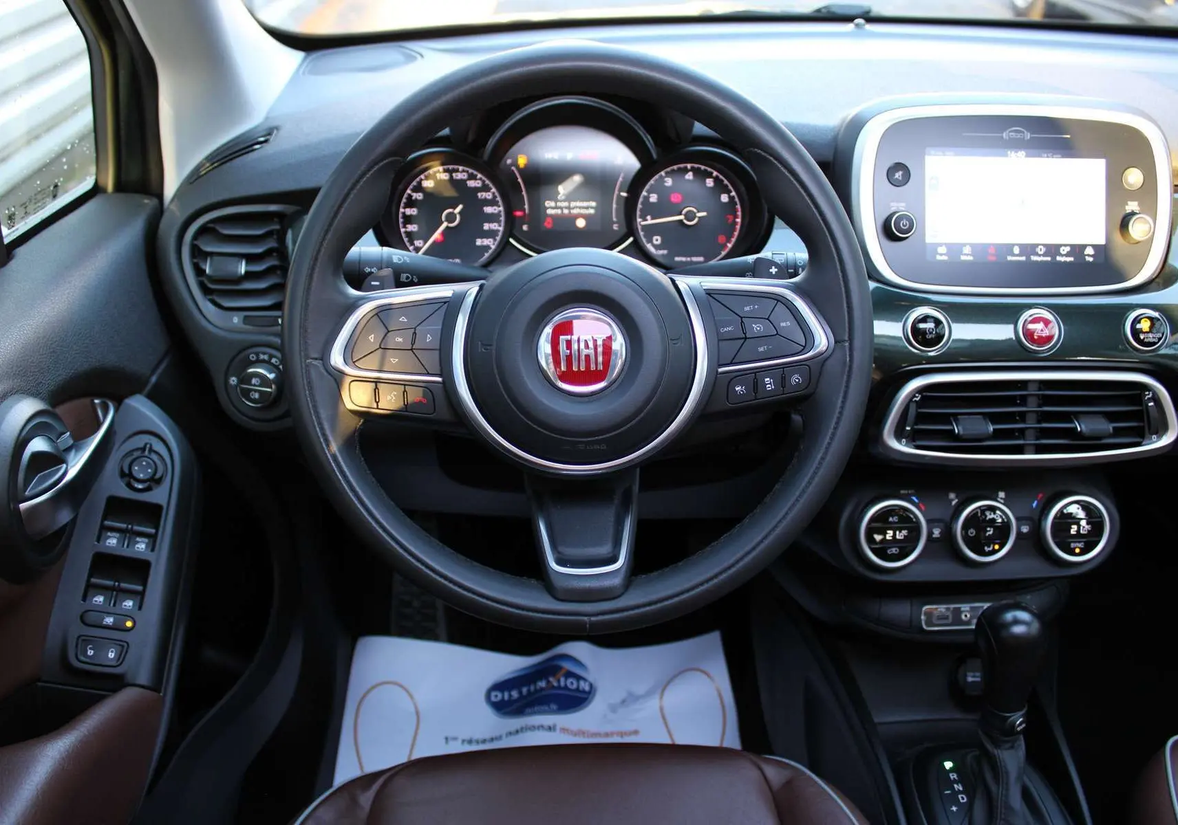 Vue intérieure centrée sur le volant et tableau de bord du Fiat 500X avec sellerie marron et écran tactile.
