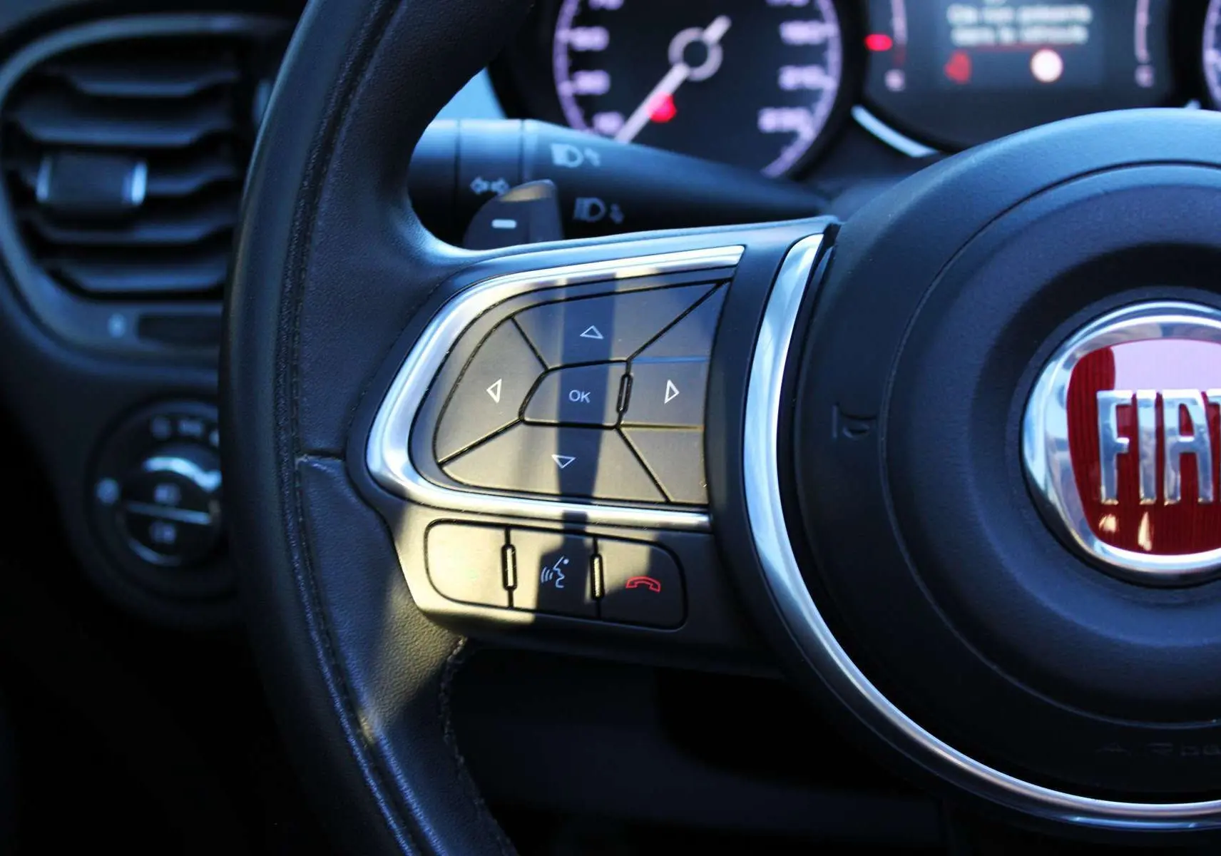 Gros plan sur le volant cuir noir de la Fiat 500X 2019, avec commandes multifonctions et logo FIAT rouge au centre.