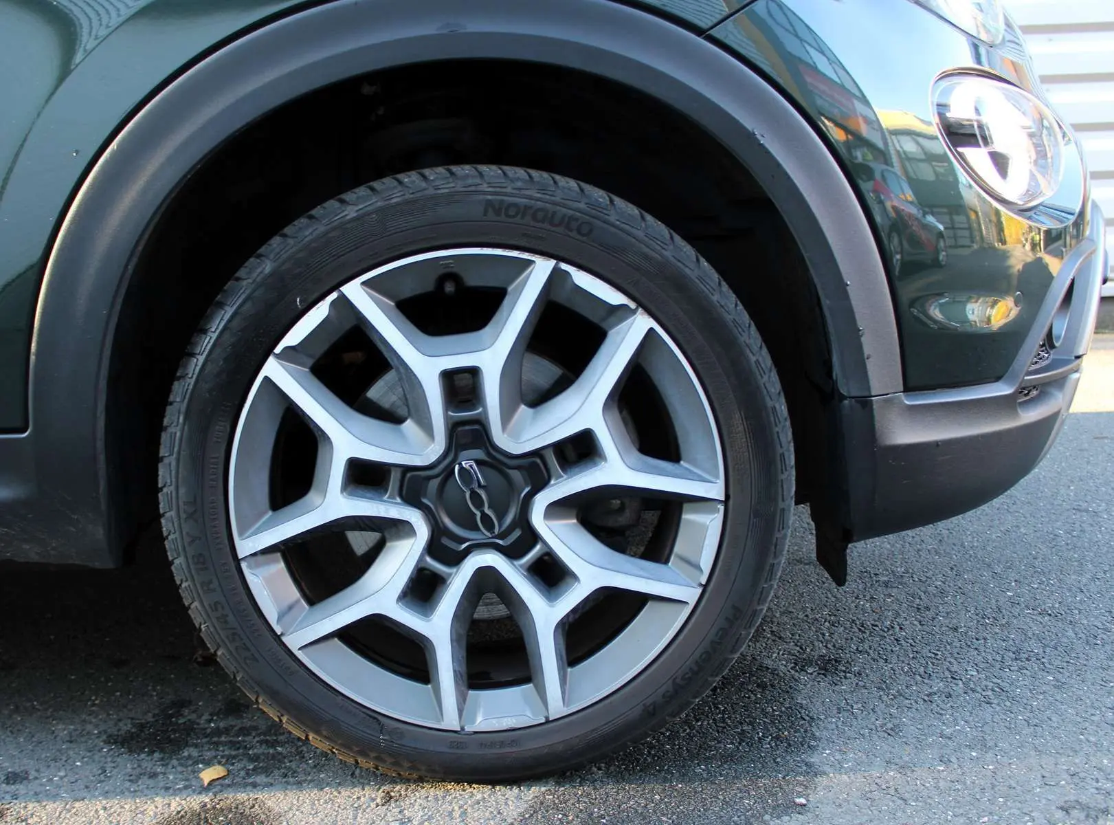 Gros plan sur la roue avant gauche d'une FIAT 500X vert Toscane métal avec jante alliage et partie avant du pare-chocs visible.
