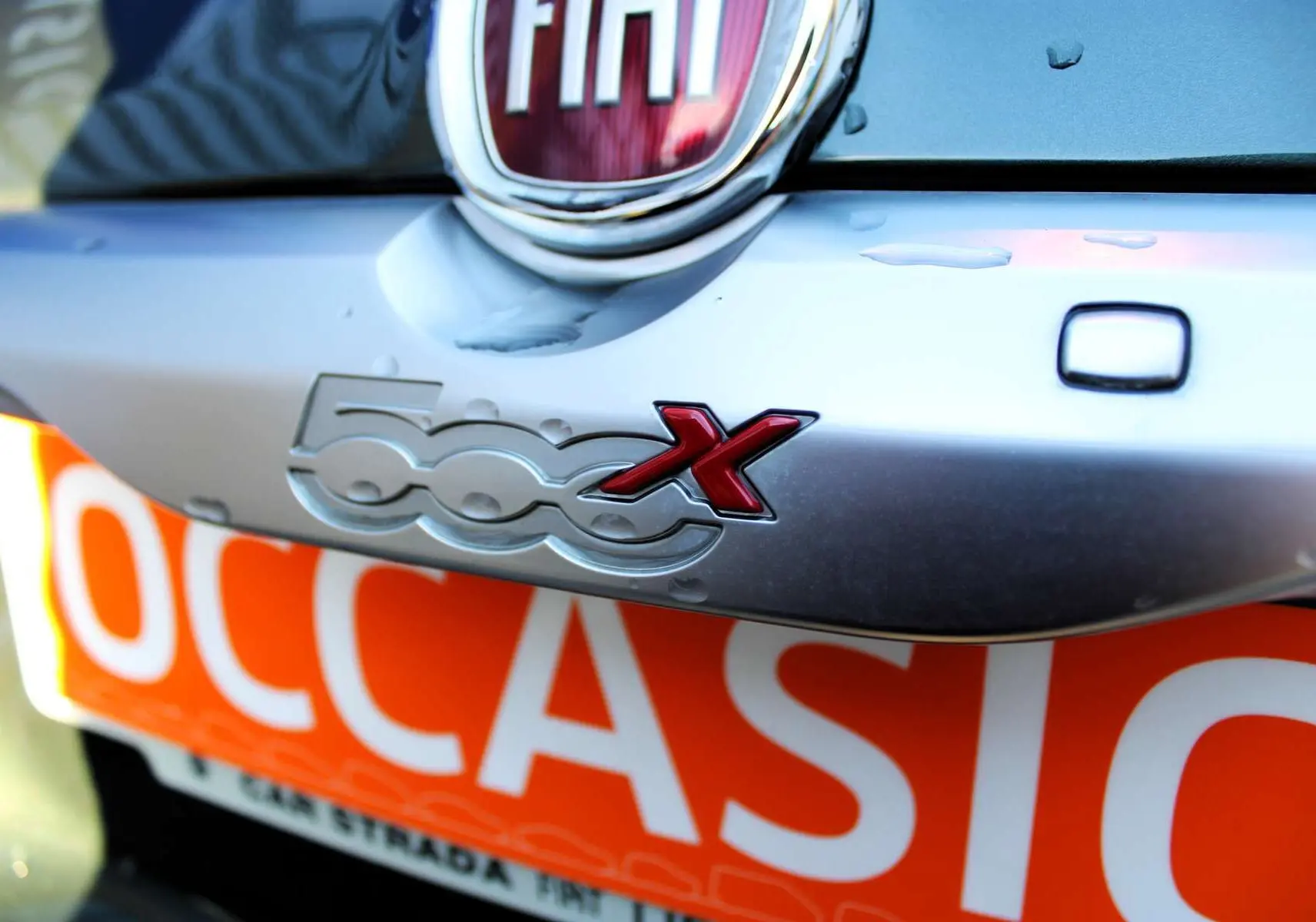 Gros plan sur le logo 500X rouge et argent à l'arrière d'une Fiat 500X vert Toscane métal.