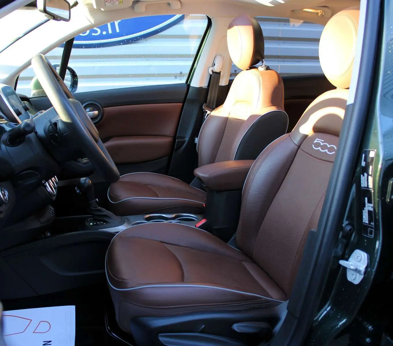 Vue intérieure côté conducteur de la Fiat 500X 2019 avec sièges cuir marron et détails verts Toscane métal.