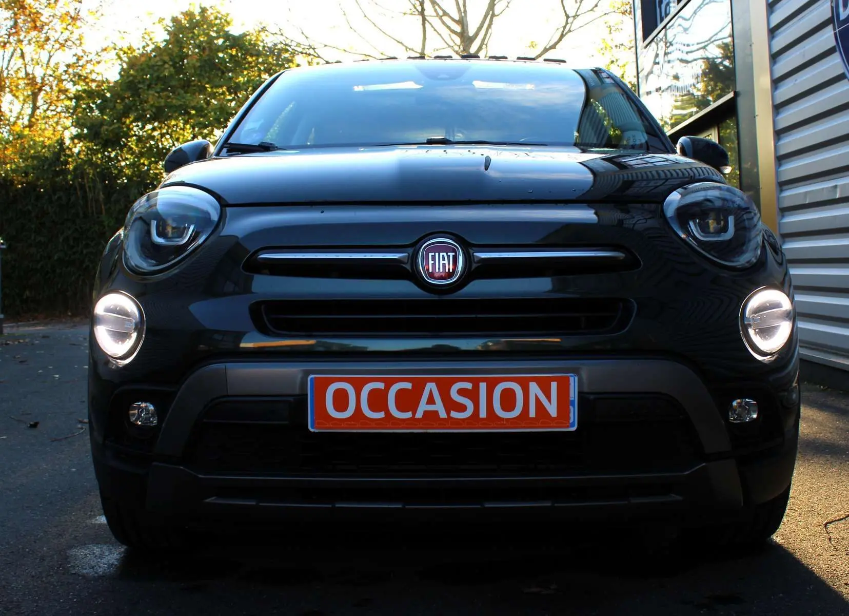 Vue frontale d'un FIAT 500X vert Toscane métal avec phares allumés et plaque "OCCASION" visible.