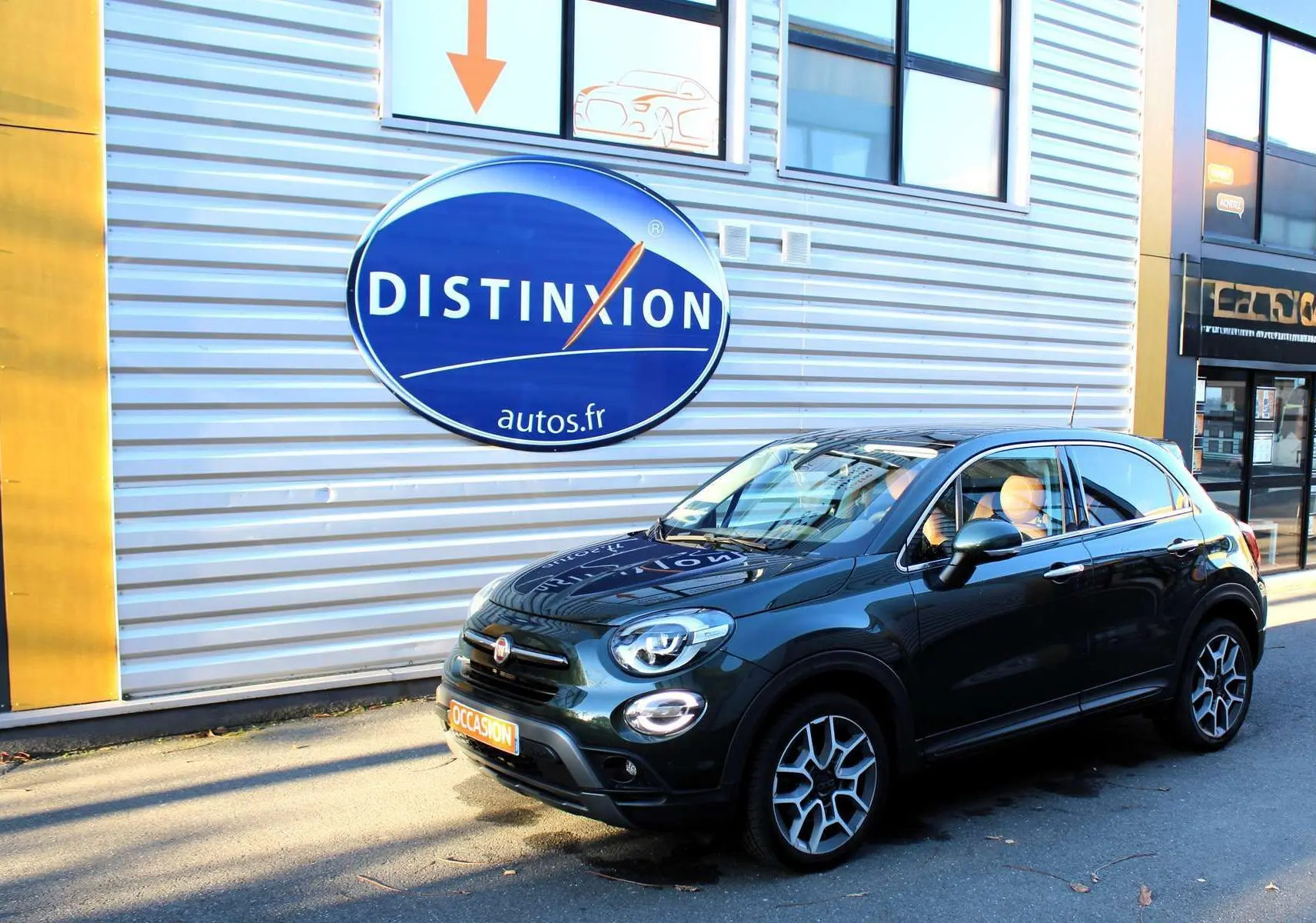 Vue 3/4 avant droit d'une FIAT 500X vert Toscane métallisé avec jantes alliage et attelage visible.