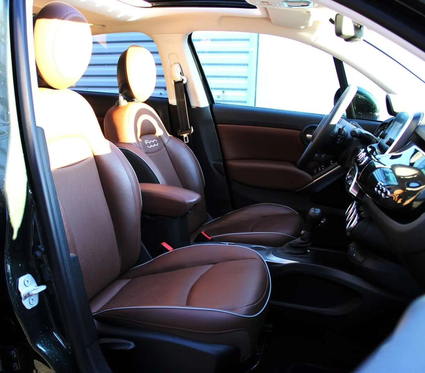 Intérieur avant droit du FIAT 500X 2019 avec sièges en cuir marron et tableau de bord noir brillant.