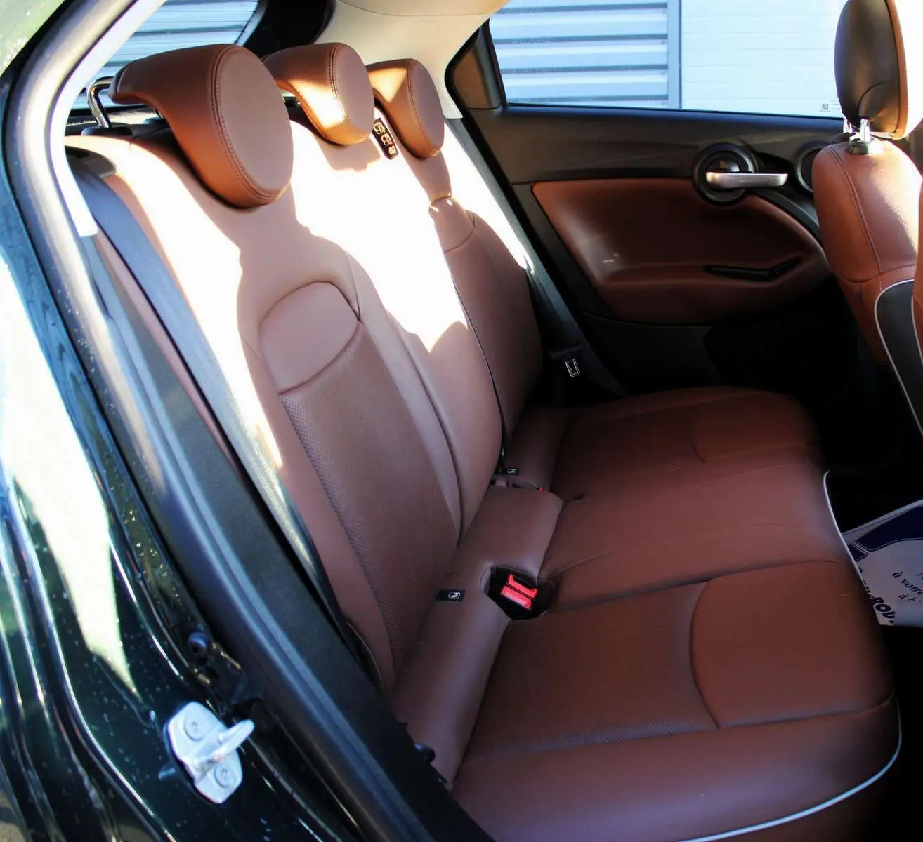 Vue intérieure arrière gauche des sièges en cuir marron du Fiat 500X 2019 vert Toscane, avec garnitures de porte assorties.