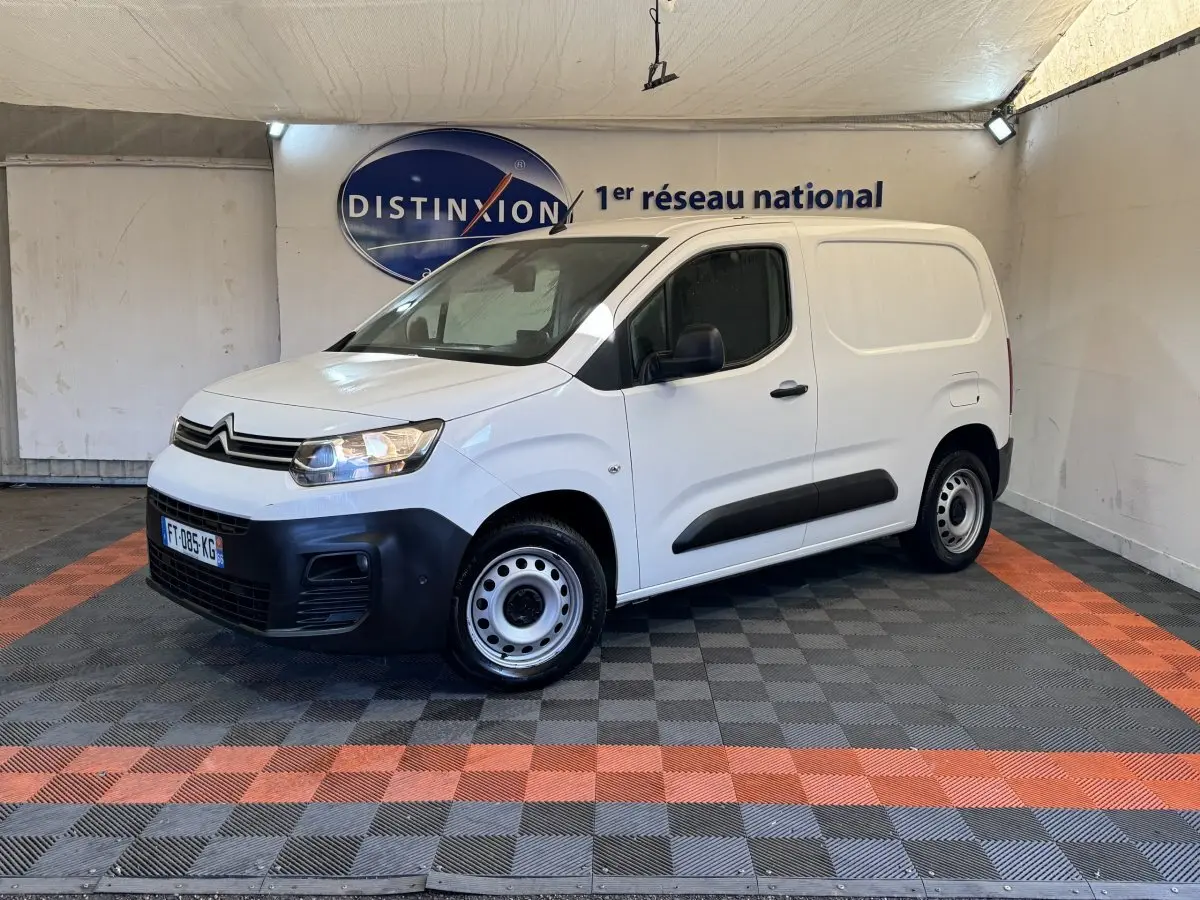 Vue 3/4 avant droite d’un utilitaire Citroën Berlingo blanc avec pare-chocs noirs et jantes acier en intérieur showroom.
