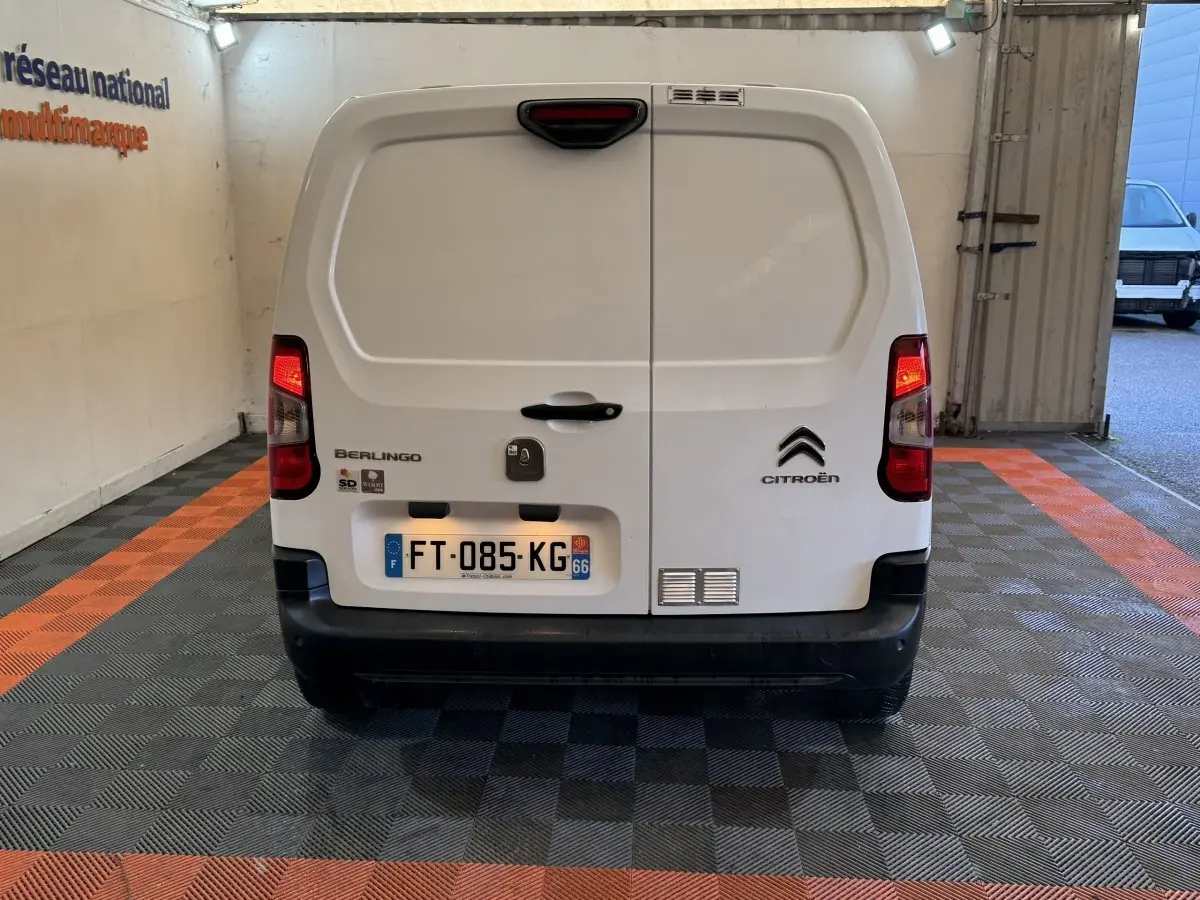 Vue arrière d’un utilitaire Citroën Berlingo blanc, avec feux arrière allumés et plaque d’immatriculation visible.