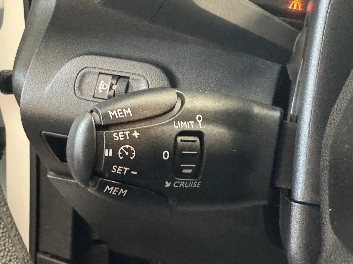 Gros plan sur la commande de régulateur de vitesse noire à gauche du volant dans l’habitacle du Citroën Berlingo blanc.