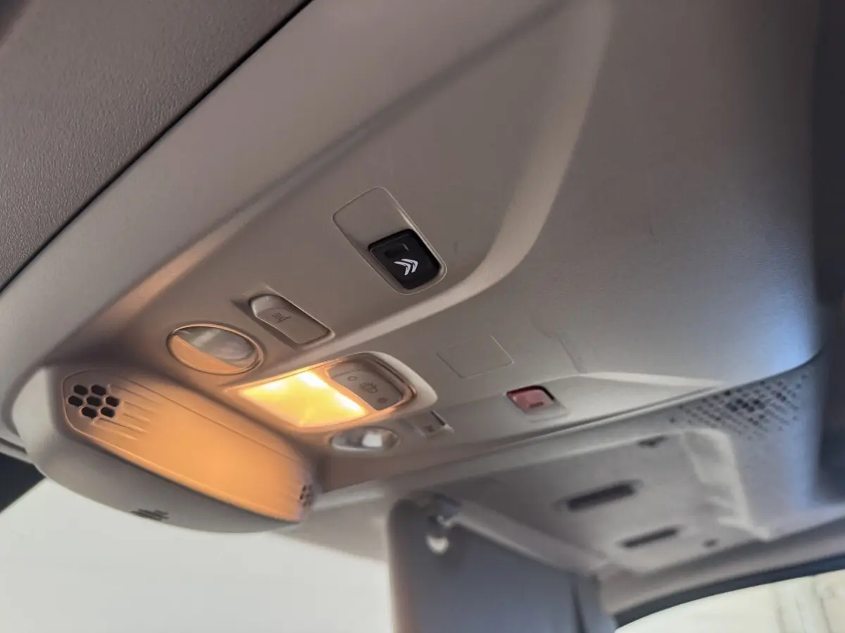 Vue intérieure en plongée sur le plafonnier gris clair du Citroën Berlingo blanc avec éclairage allumé et commandes intégrées.