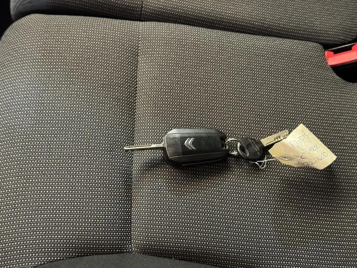 Clé de voiture Citroën posée sur un siège tissu gris foncé à motifs fins, intérieur du véhicule visible en gros plan.