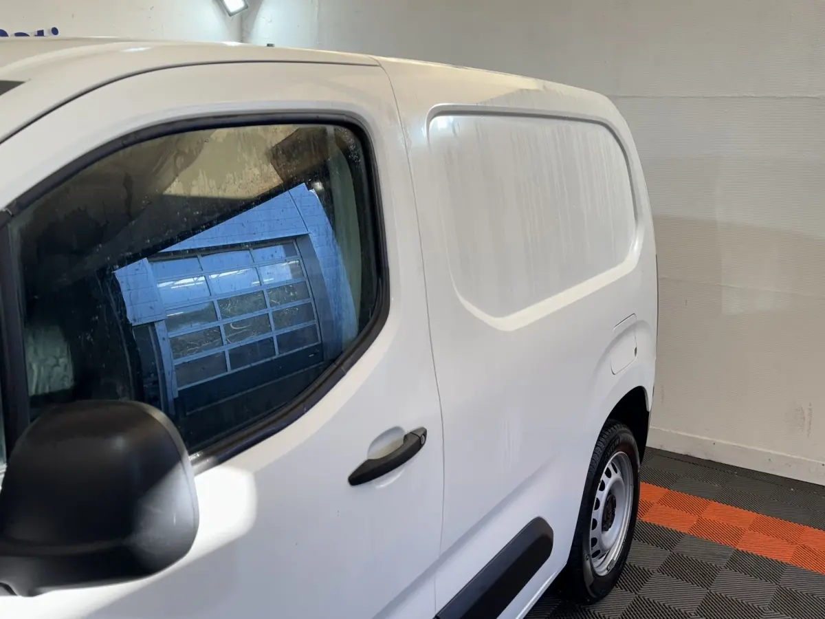 Vue de côté droit arrière d’un utilitaire Citroën Berlingo blanc avec porte latérale pleine et jante acier.