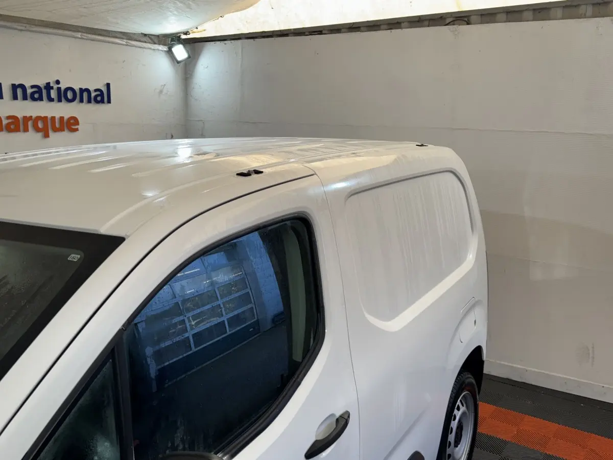 Vue 3/4 avant droit du Citroën Berlingo blanc utilitaire avec porte latérale pleine, stationné en intérieur.