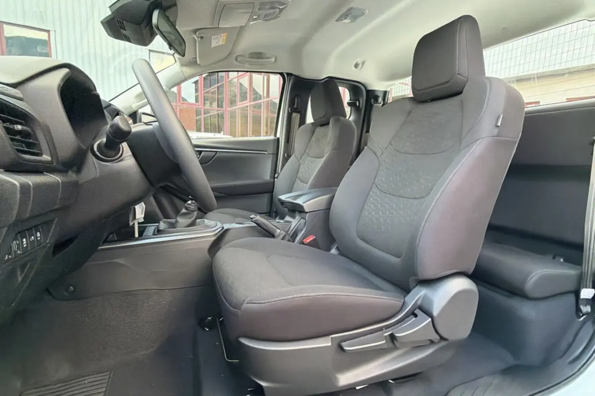 Intérieur du pick-up Isuzu D-MAX 2026, vue côté gauche sur les sièges avant en tissu gris avec accoudoir central.