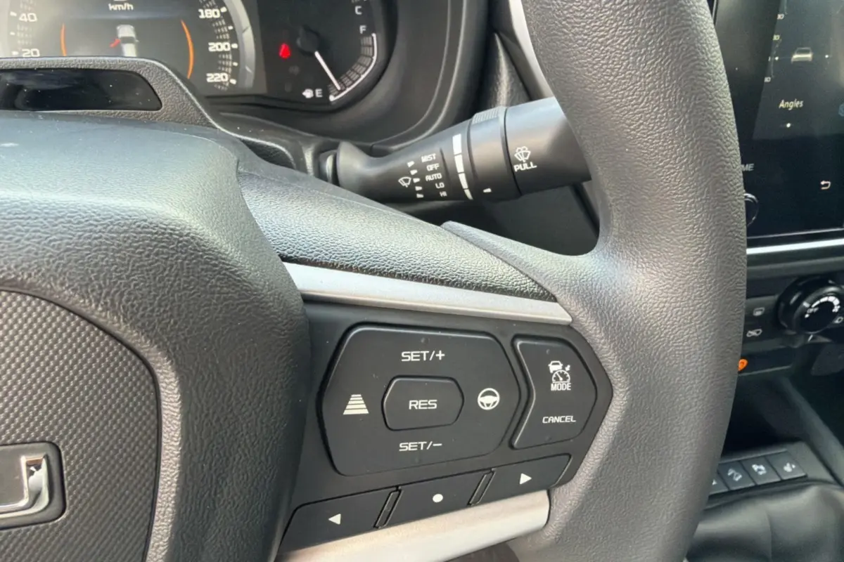 Gros plan sur le volant multifonctions noir de l'Isuzu D-MAX 2.2 TD 164 Space Evolution avec commandes de régulateur de vitesse.