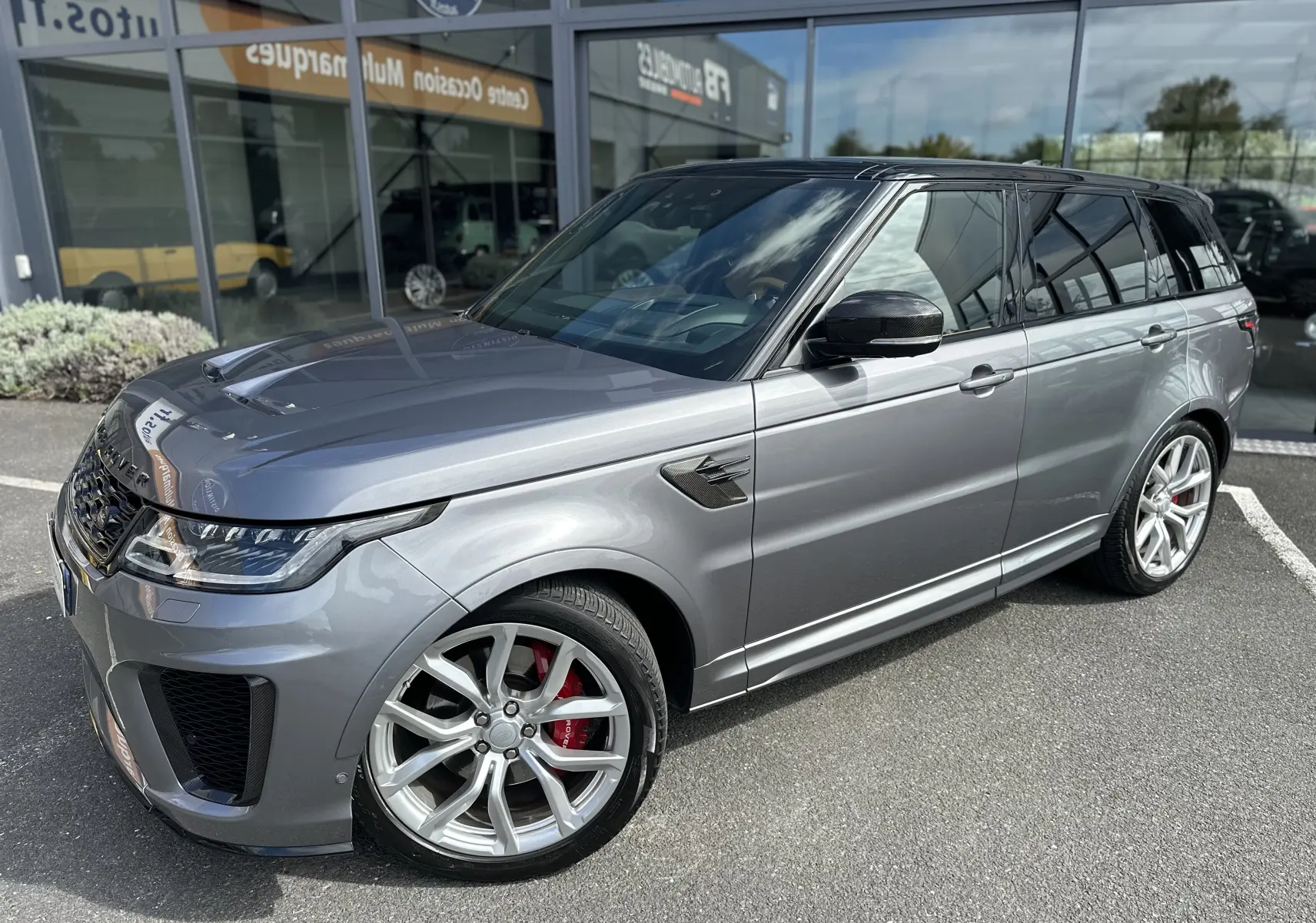 Range Rover Sport gris foncé vu en 3/4 avant droit, avec jantes alliage et étriers de frein rouges distinctifs.