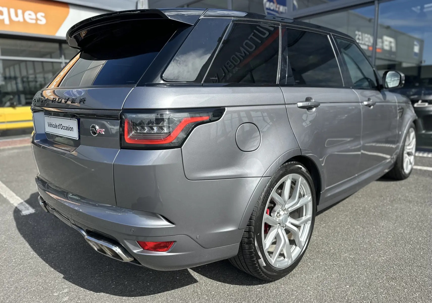 Vue 3/4 arrière droite d'un Range Rover Sport gris foncé 2020 avec jantes argentées et logo SVR distinctif.