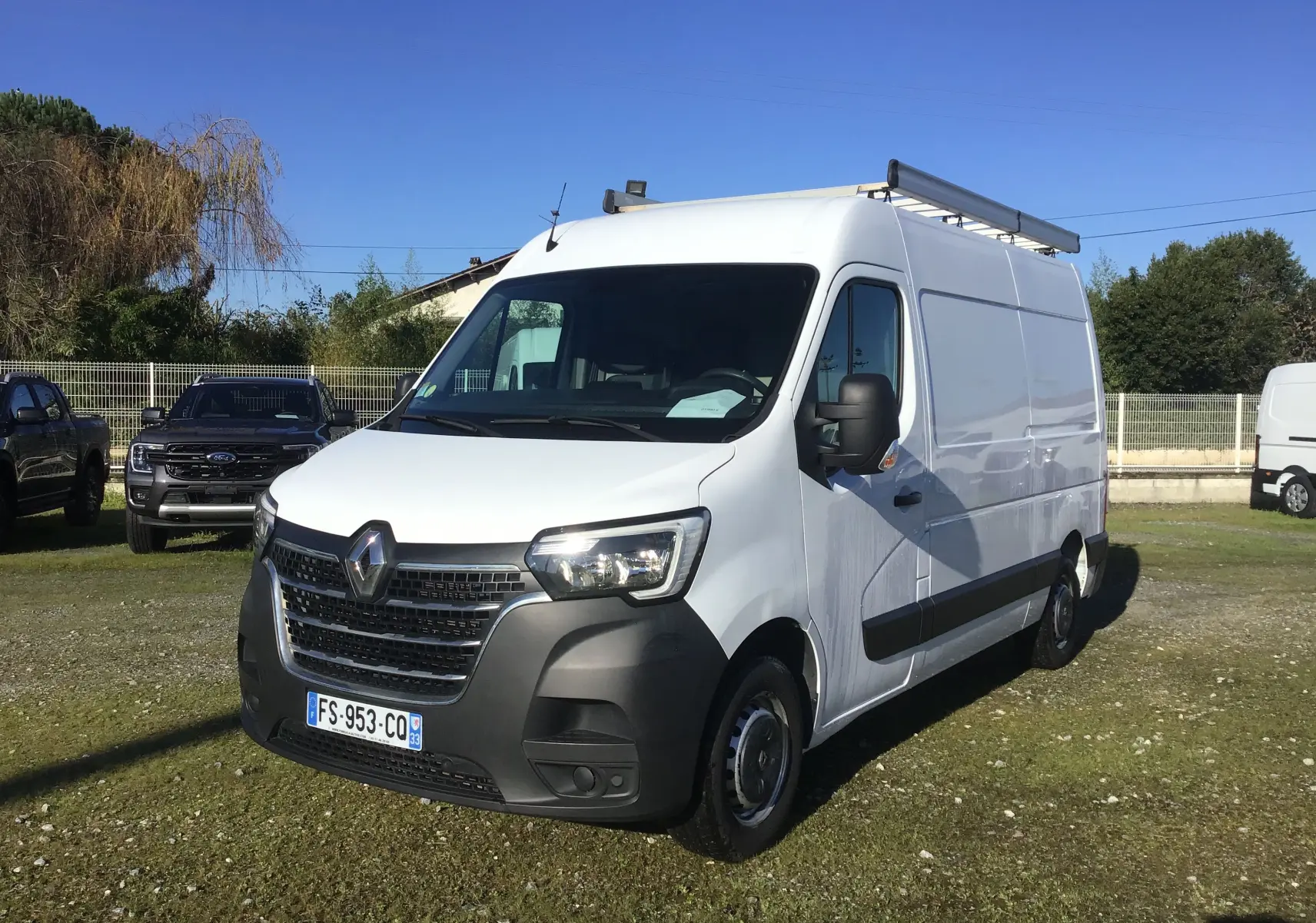 Renault Master blanc en vue 3/4 avant droit, fourgon utilitaire avec galerie de toit et rétroviseurs noirs.