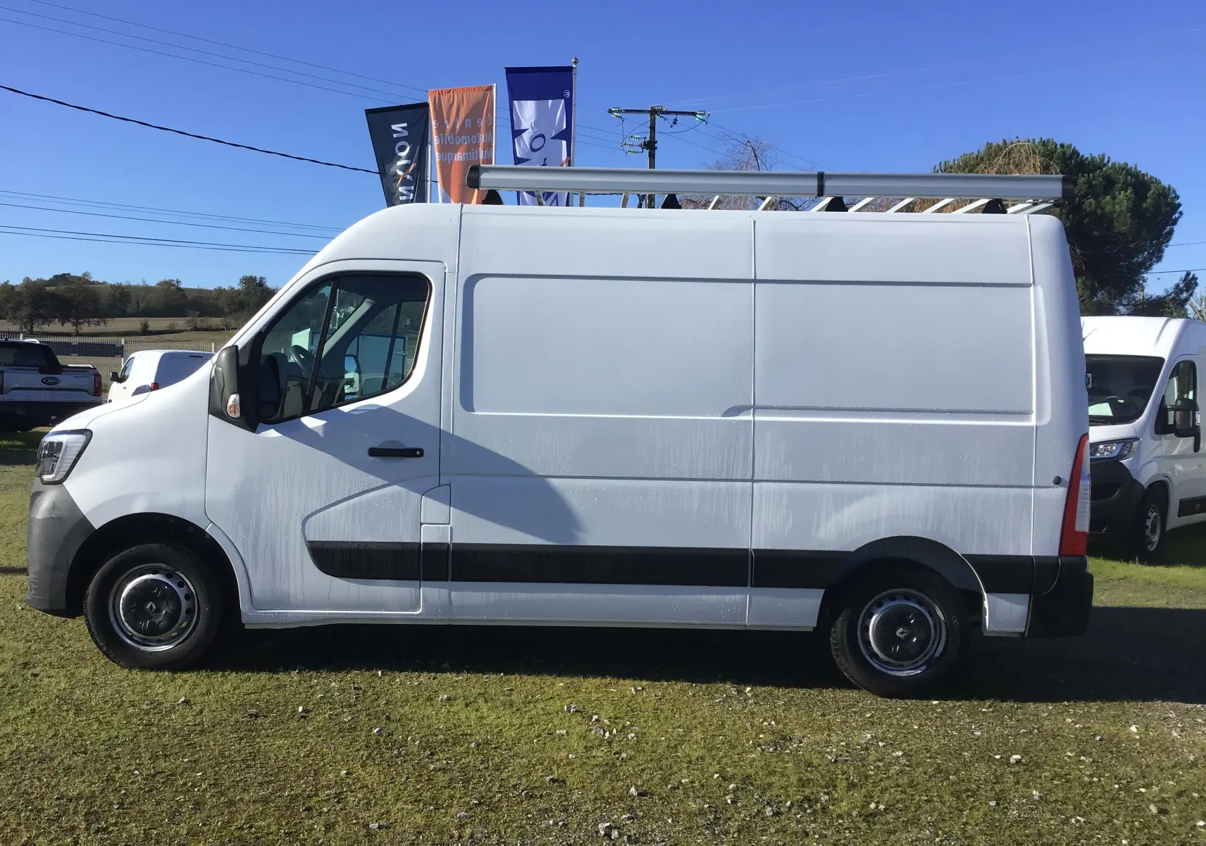Renault Master blanc en vue de profil côté gauche, avec galerie de toit et roues noires sur parking extérieur.