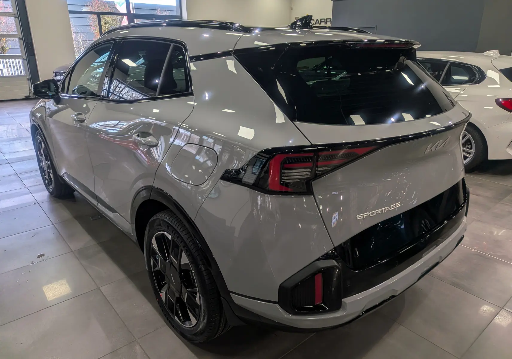 Vue 3/4 arrière droite du KIA Sportage 2025 gris céramique avec toit noir et feux arrière LED distinctifs.