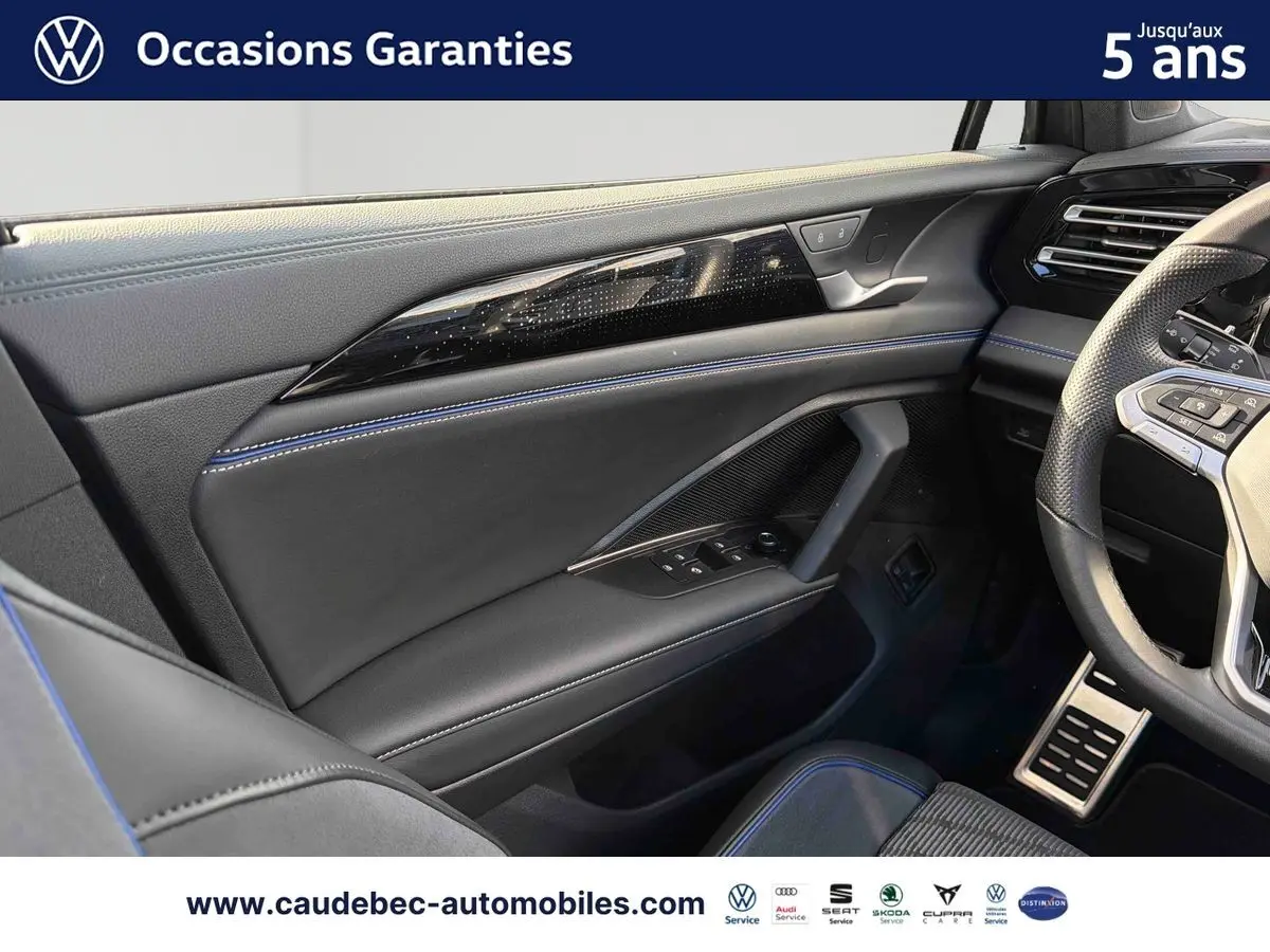Vue intérieure côté conducteur du Volkswagen Tiguan 2025, cuir noir avec surpiqûres bleues et volant sport partiel visible.
