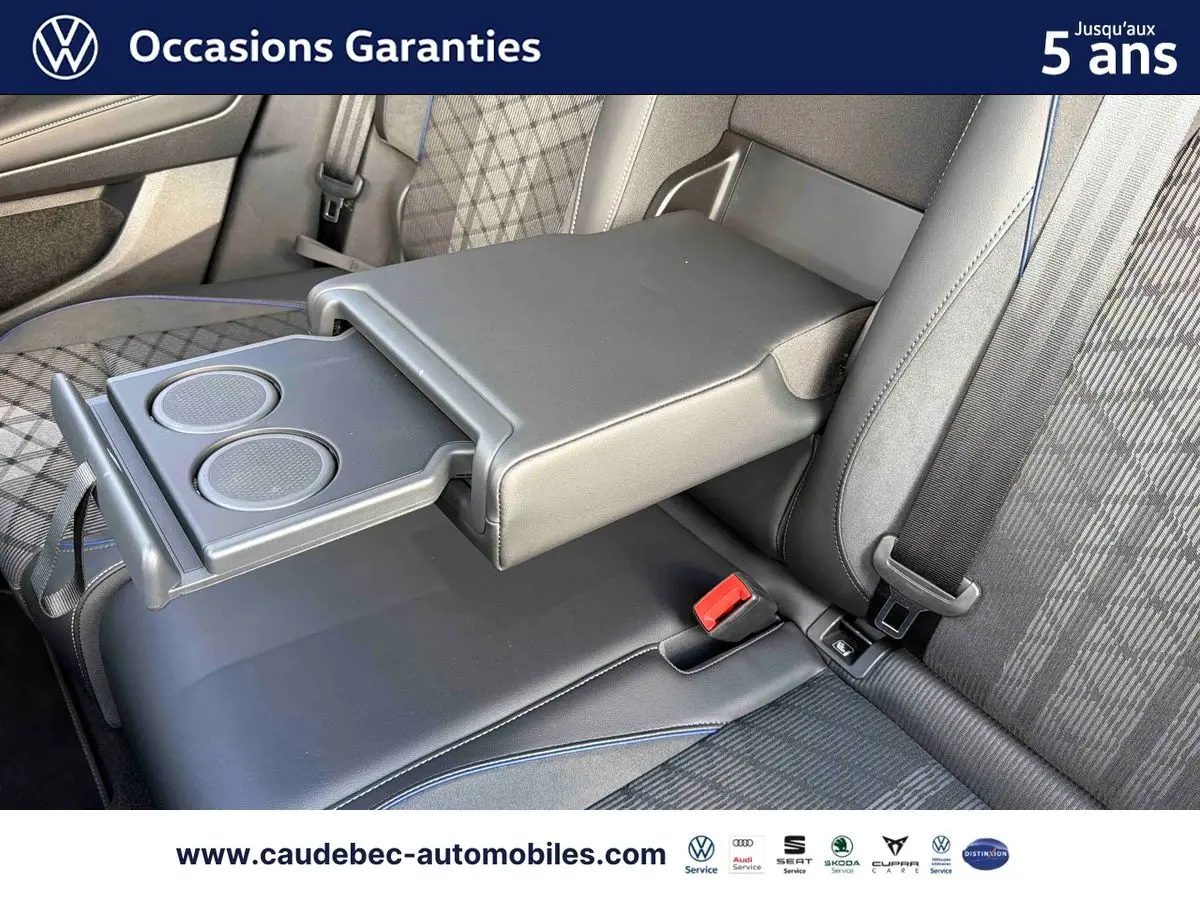 Vue rapprochée de l'accoudoir central arrière déployé avec porte-gobelets du Volkswagen Tiguan 2025, sellerie noire à motifs.