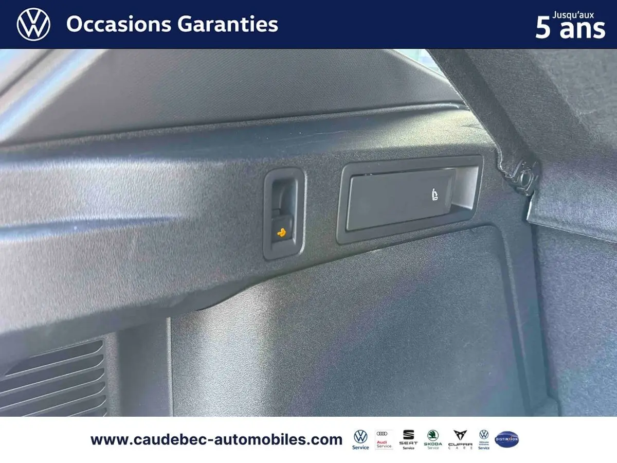 Détail intérieur du coffre du Volkswagen Tiguan eHybrid 2025 montrant les commandes de rabattement des sièges arrière.