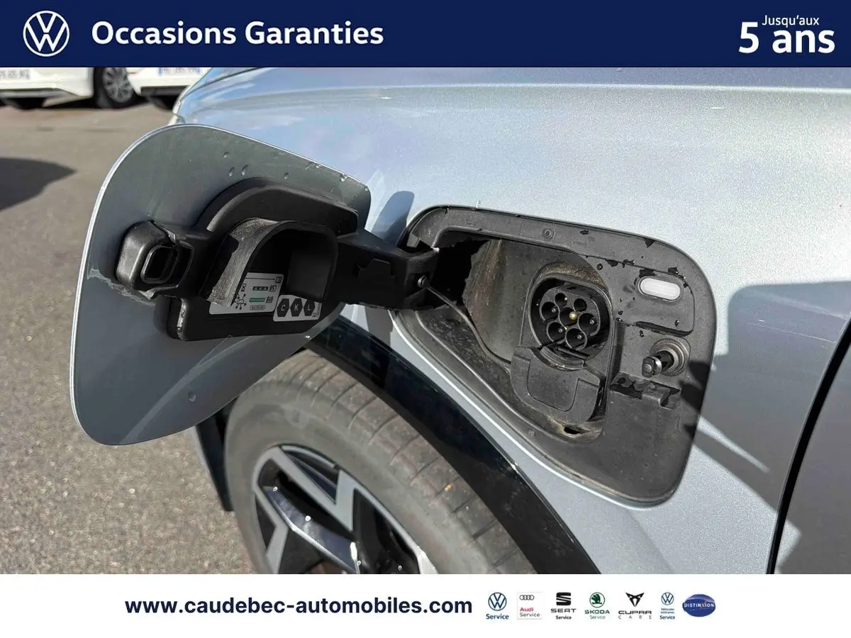 Gros plan sur la trappe de recharge avant gauche du Volkswagen Tiguan eHybrid argent Dolomite, roue et carrosserie visibles.