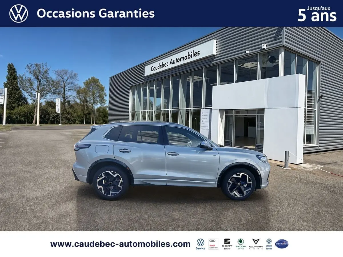 Vue latérale droite d'un Volkswagen Tiguan 2025 argent Dolomite avec jantes alliage et toit panoramique, devant un concessionnaire.