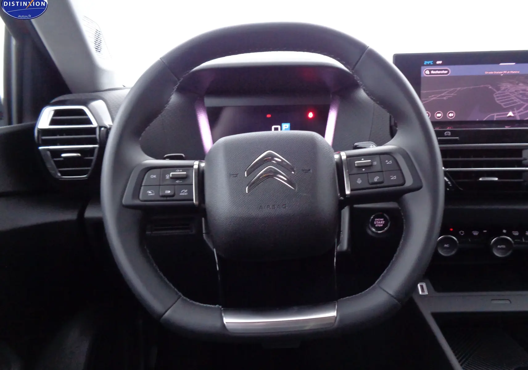 Vue rapprochée du volant cuir noir de la Citroën C4 X 2023 avec commandes intégrées et écran tactile en arrière-plan.