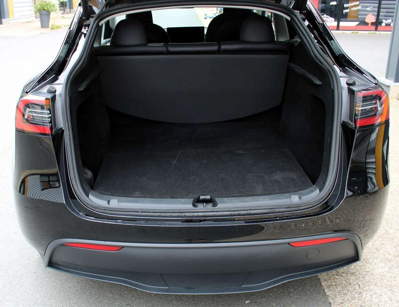 Coffre ouvert vu de l'arrière d'une Tesla Model Y noire métal 2024, soulignant l'espace de chargement vide et le hayon relevé.