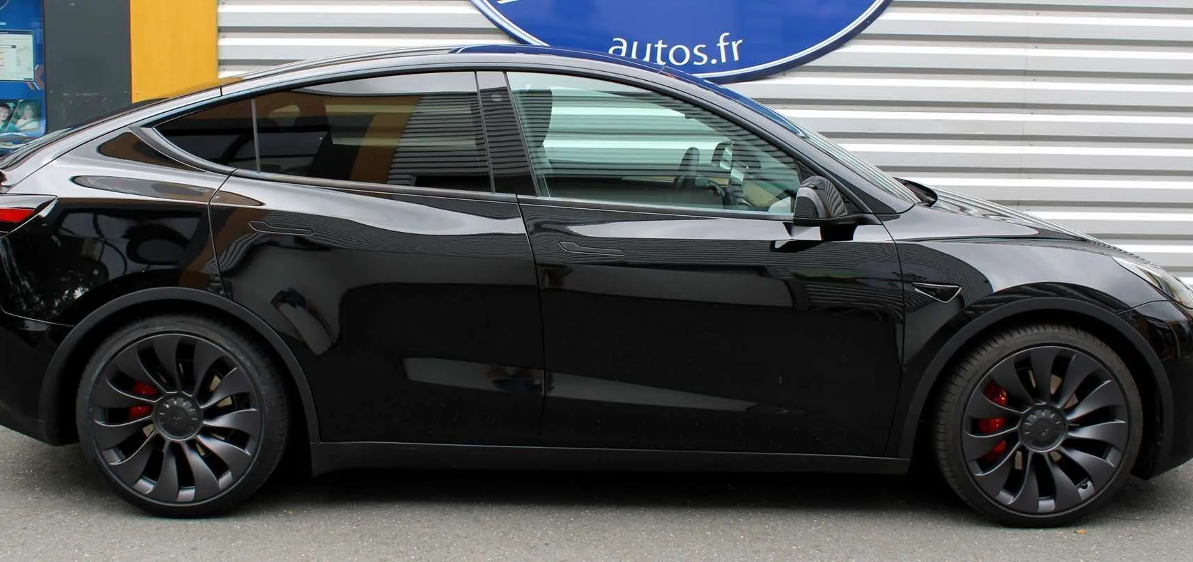 Tesla Model Y noir métal vue de profil côté gauche, avec jantes noires et étriers de frein rouges visibles.
