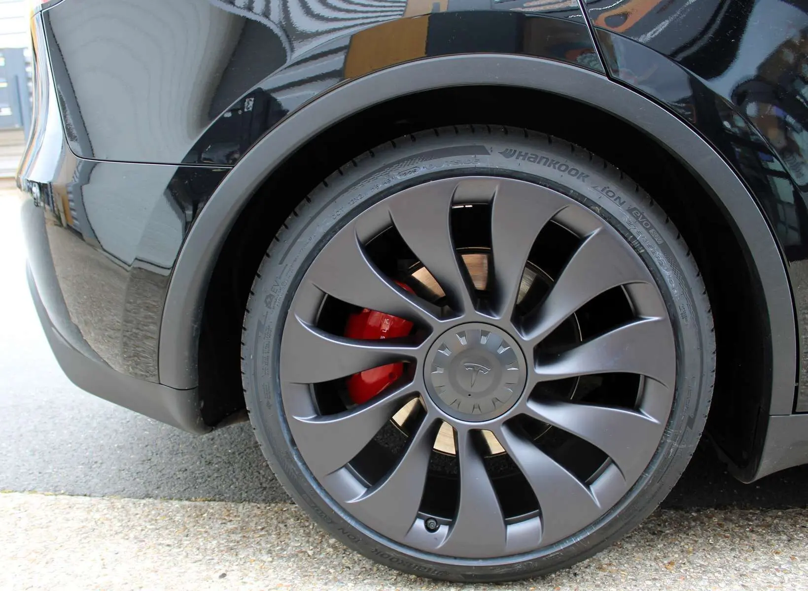 Gros plan sur la roue arrière droite noire métallisée d'une Tesla Model Y 2024 avec étrier de frein rouge visible.