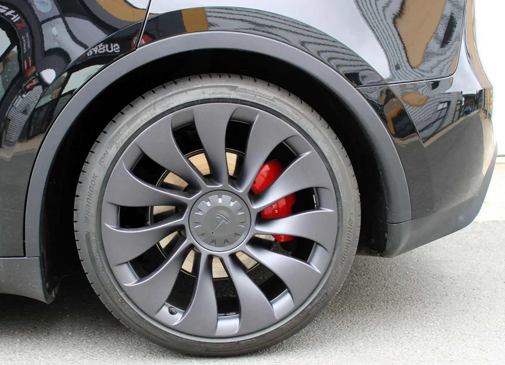 Gros plan sur la roue arrière droite noire métallisée d'une Tesla Model Y 2024 avec étrier de frein rouge visible.