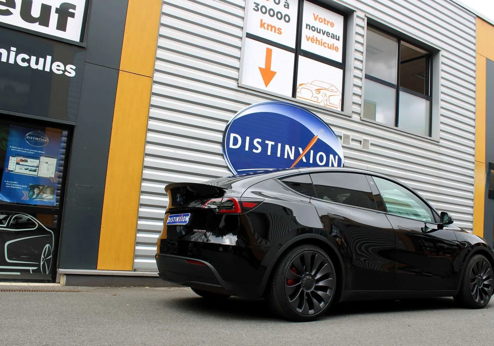 Tesla Model Y Performance noir métal en 3/4 arrière droit, stationné devant un bâtiment avec enseigne Distinxion.